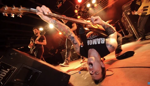 Musician performing a backflip while playing guitar on an illuminated stage.