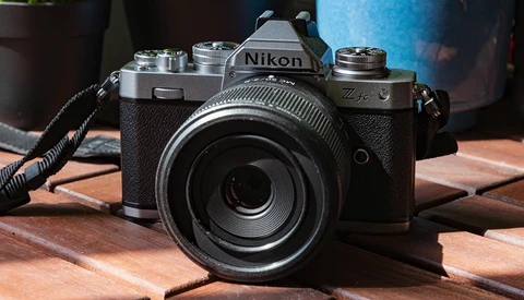 Nikon Z fc mirrorless camera with attached lens on wooden surface, with camera strap and blue container in background.
