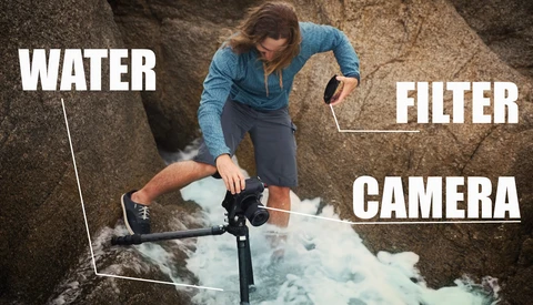 Photographer in blue jacket demonstrating underwater camera setup with water, filter, and camera labeled in rocky environment.