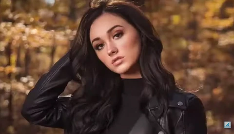 Woman with long dark hair wearing a black leather jacket against a golden bokeh background.