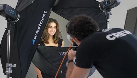 Portrait photographer shooting a female subject in a professional studio setup with softbox lighting and reflectors.