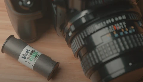 Film canister and camera lenses arranged on wooden surface.