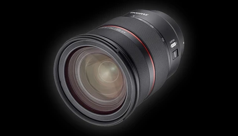 Professional camera lens with red accent ring, displayed against black background with dramatic lighting.
