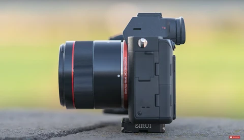Mirrorless camera with wide-angle lens mounted on a tripod plate, photographed from the side against a blurred green background.