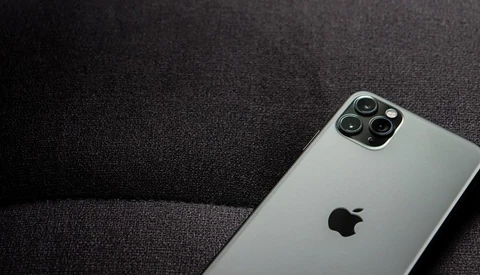 Silver iPhone with quad camera system positioned on dark textured fabric surface.