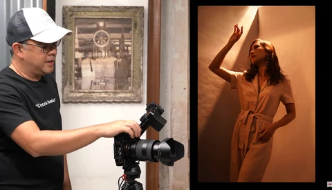 Photographer operating a mirrorless camera on tripod while model poses in warm studio lighting.