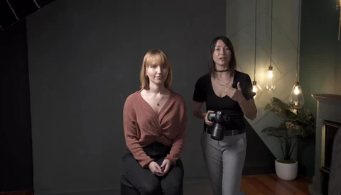 Two women in a modern indoor studio space with pendant lighting and plants in the background.