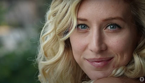 Blonde woman with wavy hair smiling at camera in natural outdoor light.