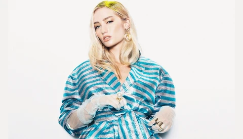 Person wearing blue and gray striped wrap top with blonde hair and gold hoop earrings against white background.