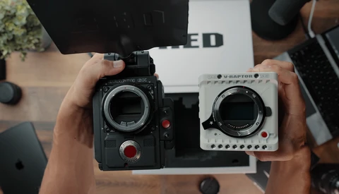 Two cinema cameras held side-by-side for comparison, one black and one white, both displaying their lens mounts and control interfaces.