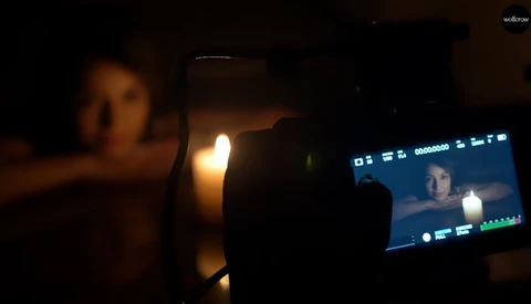 Mobile phone recording video in low-light setting with warm ambient lighting and a monitor displaying the live feed.