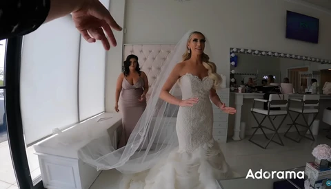 Bride in beaded wedding dress with flowing veil being adjusted during bridal preparation in salon.