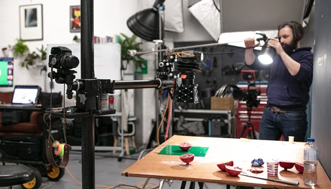 Cinematographer operating a camera on a jib arm in a studio with food photography setup below.