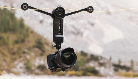 Gimbal-mounted camera rig suspended in air with mountainous landscape below.