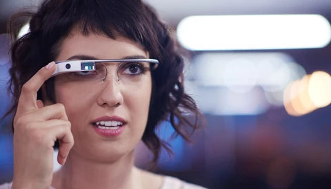 Woman wearing smart glasses with her finger on the frame, smiling at camera.