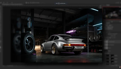 Silver Porsche 911 in a garage workshop with neon lighting and a large wheel display on the left wall.