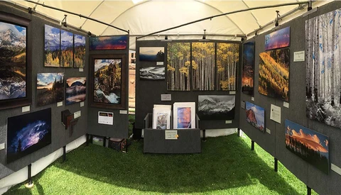 Photography exhibition tent with landscape images displayed on dark panels and central pedestals.