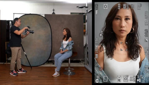 Portrait monitor display showing a woman's headshot while a photographer adjusts a large circular reflector during a studio portrait session.