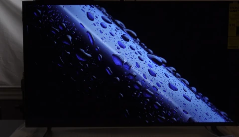 Water droplets on a blue cylindrical surface against a dark background, angled diagonally across frame.