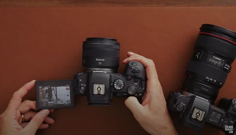 Overhead view of Canon camera bodies and lenses arranged on rust-colored background with hands positioning equipment.