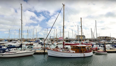Marina filled with sailboats moored at docks under partly cloudy sky.