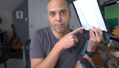 Man in a gray t-shirt demonstrating a photography lighting modifier with a white diffusion panel.