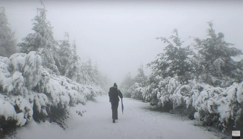Solitary figure jogging through a snow-covered evergreen forest in heavy fog.