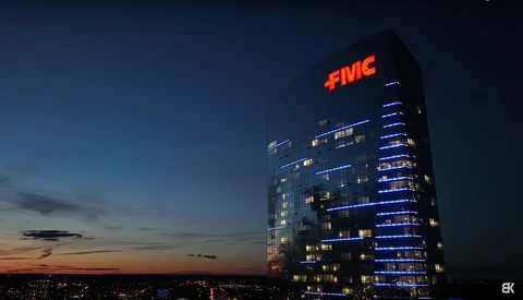Illuminated office tower at dusk with red FMC sign glowing against twilight sky.