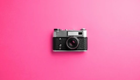 Vintage rangefinder camera with chrome top plate and black body on bright pink background.
