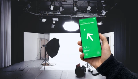 Hand holding green smartphone displaying navigation app with directional arrow in professional studio setting.