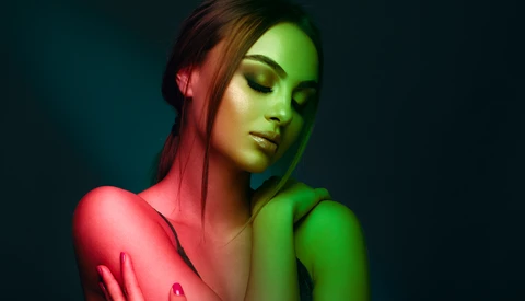 Portrait of a woman with dramatic split-color gel lighting in red and green against a dark teal background.
