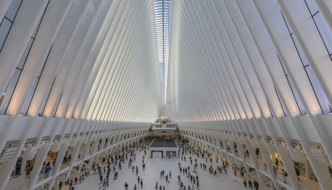 Interior of the Oculus transit hub with symmetrical white ribbed ceiling and crowds of people in the floor-level concourse.