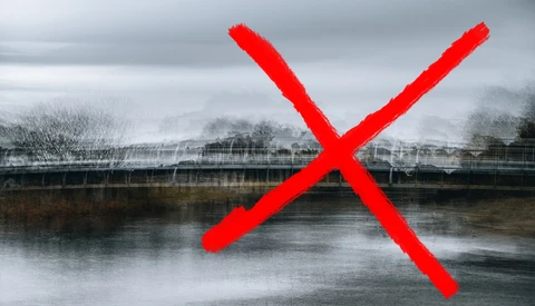 River landscape with bare trees and overcast sky marked with a large red X.