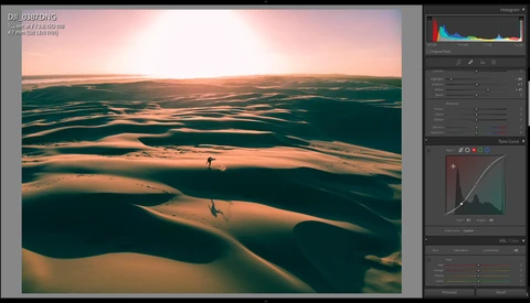 Aerial view of sand dunes with two figures walking across the rippled landscape at golden hour.