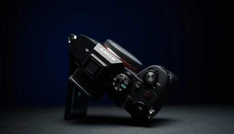 Black film camera tilted at an angle against a dark blue background with dramatic side lighting.