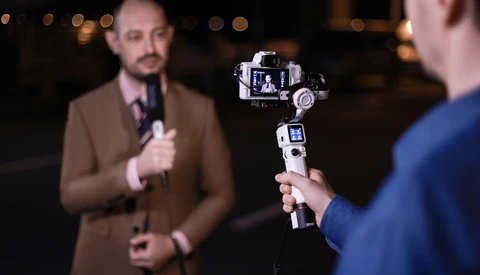 Man holding a smartphone gimbal stabilizer with mounted camera during evening interview.