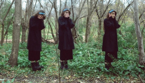 Three people in burgundy coats arranged in a triptych, adjusting their hats in a bare forest.