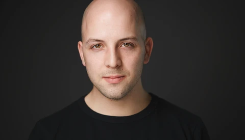 Portrait of a bald man with a neutral expression against a dark background.