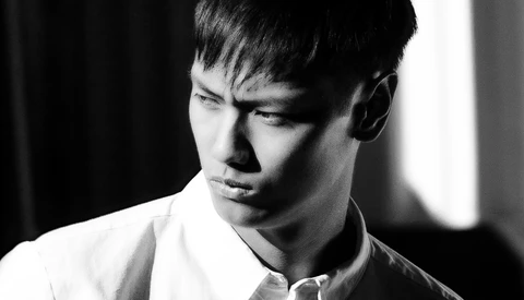 Portrait of a young man in a white shirt, shot in black and white with dramatic side lighting.