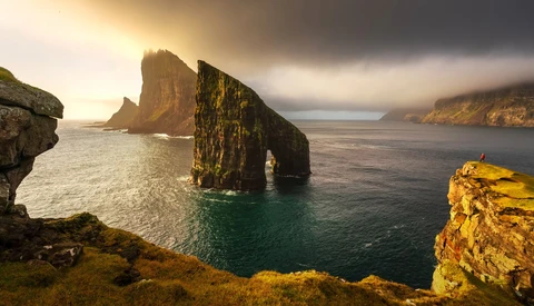 Dramatic coastal landscape with tall sea stacks rising from ocean and moss-covered cliffs bathed in golden light.