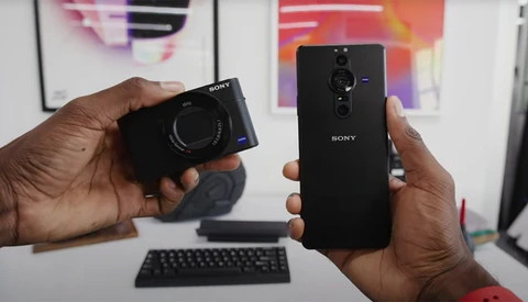 Hands holding a Sony compact camera and Sony smartphone side by side for comparison.