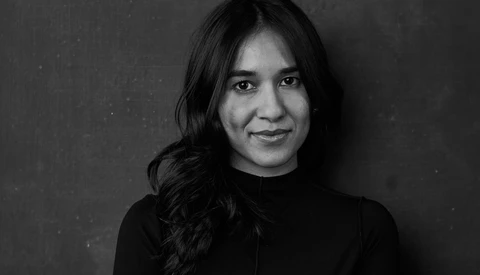 Black and white portrait of a woman with long dark hair wearing a dark turtleneck against a neutral background.