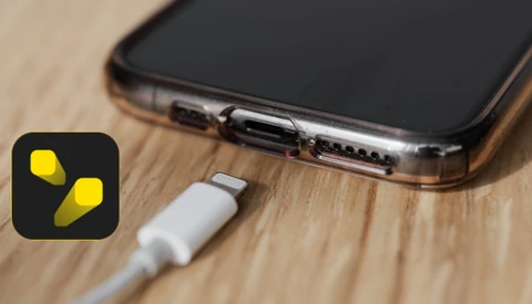 Lightning connector cable plugged into smartphone charging port on wooden surface.