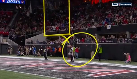 Football stadium field with players and officials during a game, with yellow circle highlighting an area near the sideline.