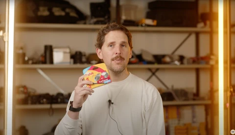 Man holding a colorful patterned object while looking upward in a studio setting with wooden shelving.