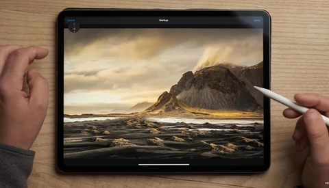 iPad displaying a dramatic Icelandic landscape with a dark mountain peak, black sand beach, and golden-hour lighting, being edited with an Apple Pencil.