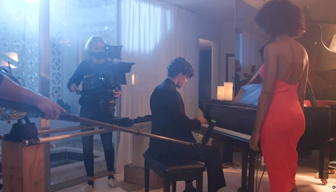 Cinematographer operating a camera while woman in red dress stands nearby during what appears to be a film or television production shoot.