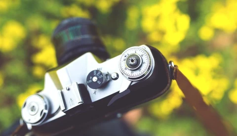 Vintage rangefinder camera with chrome lens and black body displayed against blurred yellow-green foliage background.