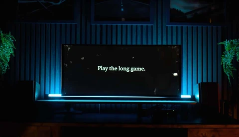 Large screen displaying white text reading 'Play the long game' against a black background, illuminated by blue accent lighting.