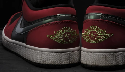 Rear view of burgundy and black high-top sneakers with gold winged logo embroidery on heel tabs and white sole.